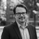 Black and white portrait of Patrick A. in a suit and glasses.