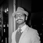 Black and white photo of Anand C. wearing a hat and glasses.