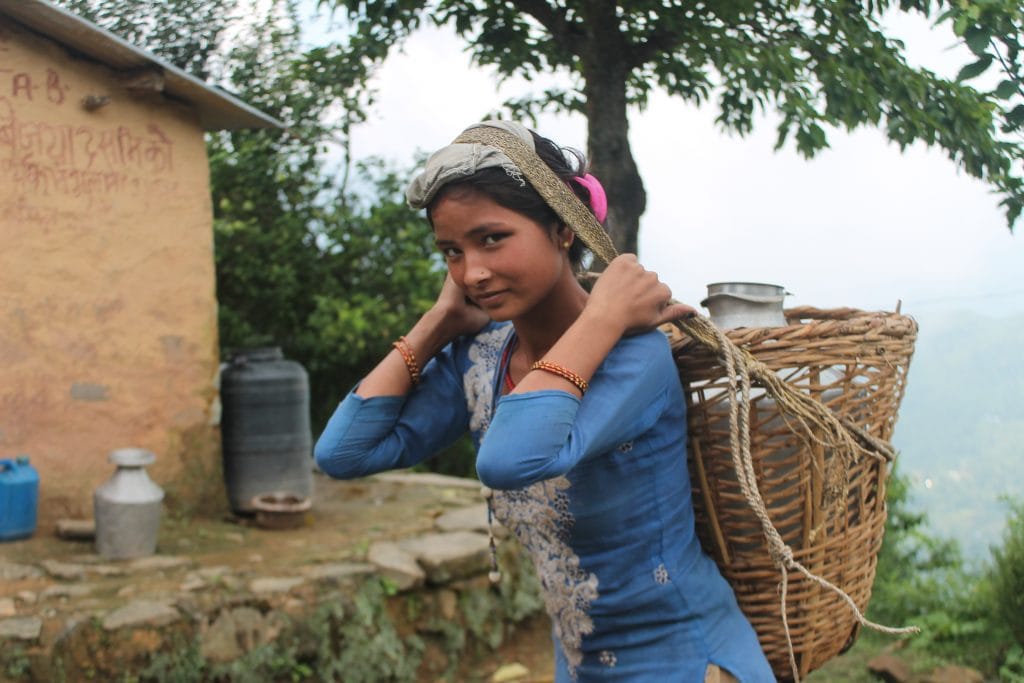 Young Nepali woman carrying a basket on her back with a large vessel of water 