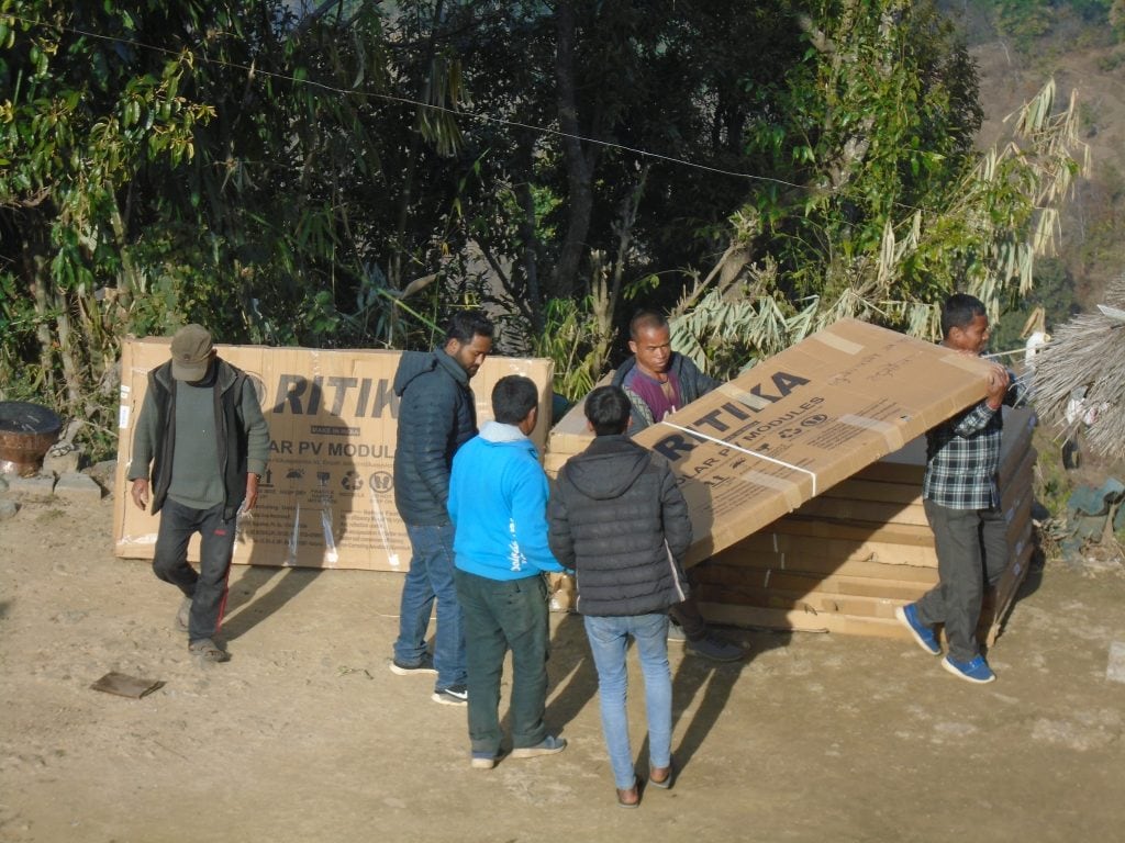 Boxes of large solar panels on the ground being moved by community members 