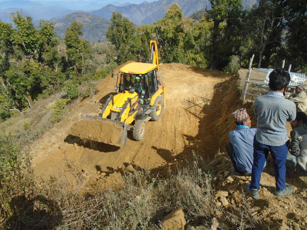 Community members watching a yellow JCB digger flattening land in preparation for the installation of the solar aray