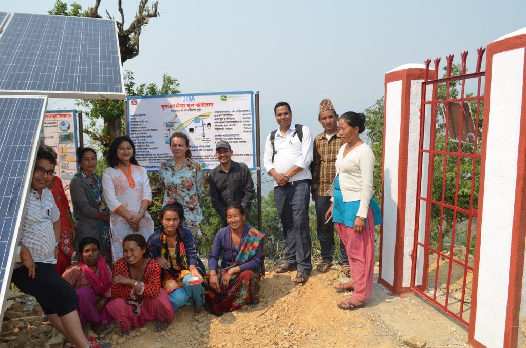 A group of community members smiling and standing next to the solar panels. 