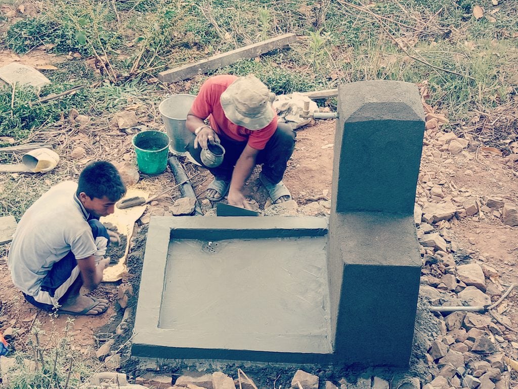 Two masons constructing a water thank with water collection point