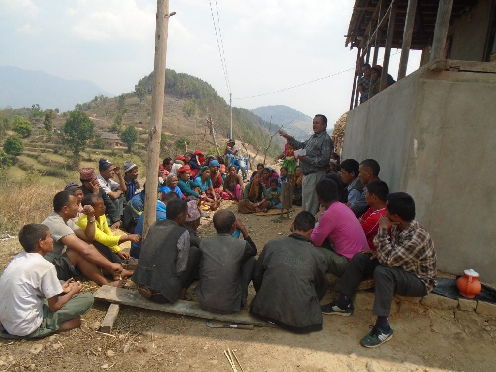 Community members sitting on the ground taking part in a community meeting