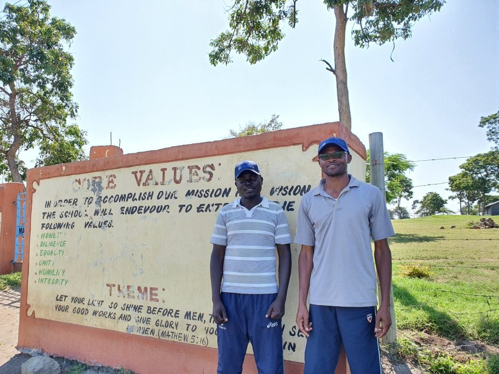 Fred, the deputy head pictured on the left, standing outside the school gates. He is now completing a distance learning course in Business Administration, which will help him to better support the school going forward