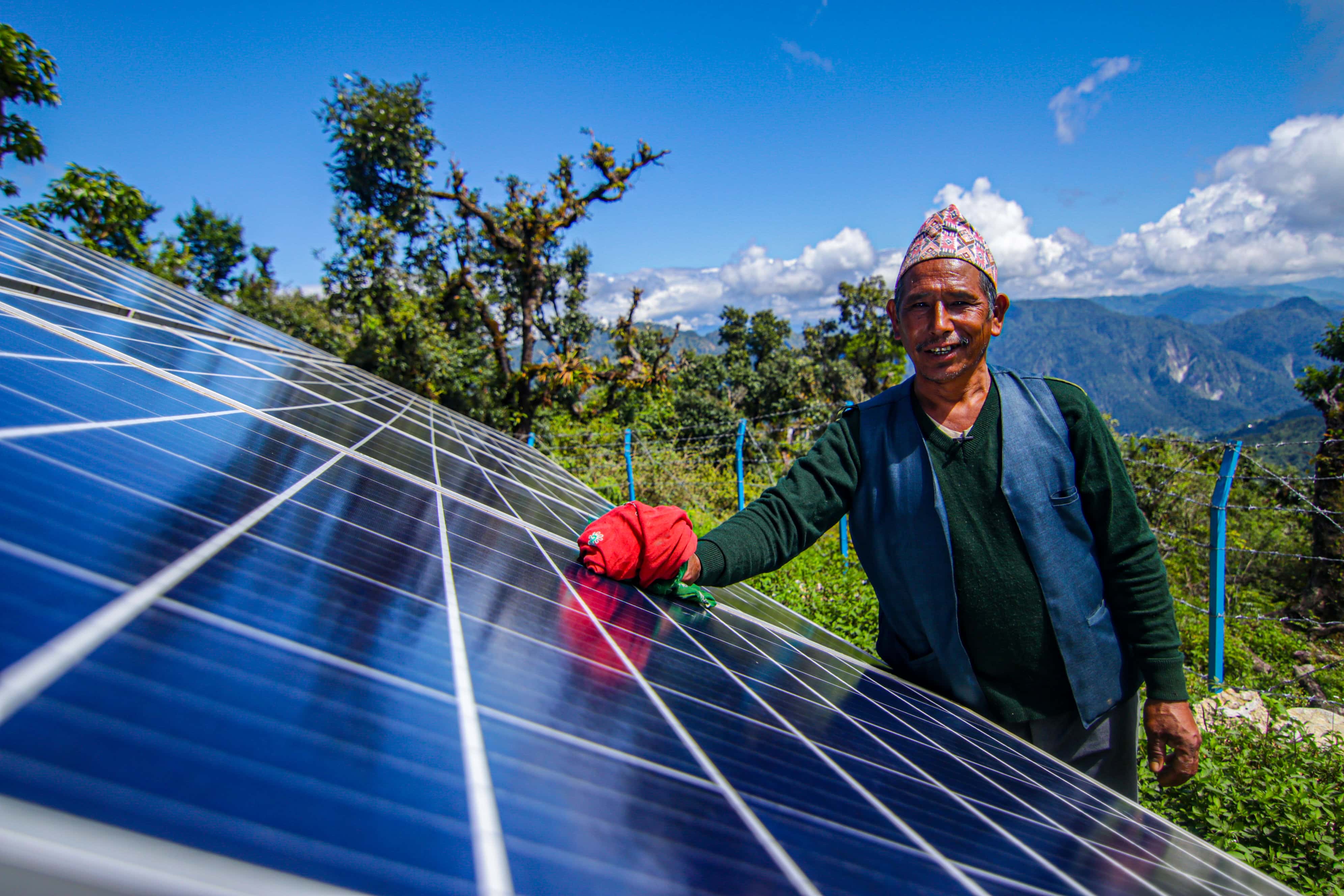 A Nelapi man cleaning an array of solar panels that are used to lift water to hilltop communities. In the background you can see the mountains that form this hilly terrain.