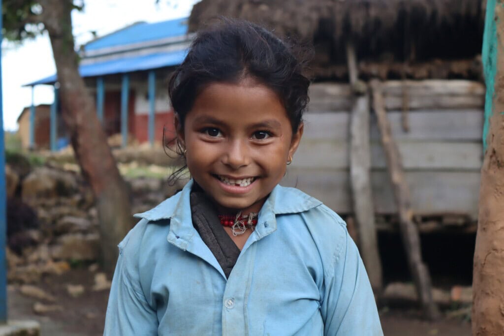 A close up of Manisha Budha wearing school uniform, she is looking straight at the camera and beaming.