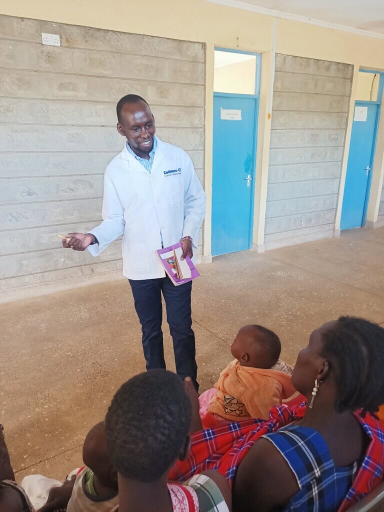 A Kenyan nurse is speaking to two female patients, both holding babies, inside a rural health clinic that now has its own solar energy system