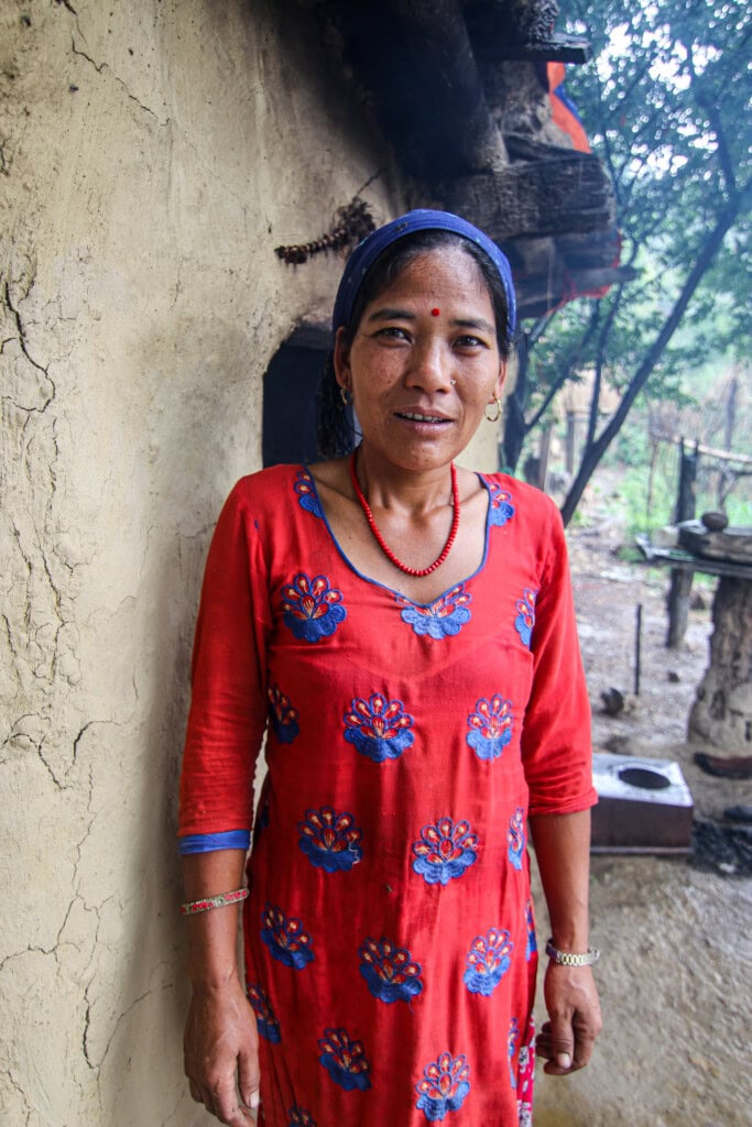 A Nepali women dressed in a red tunic standing outside her home in a rural part of Nepal