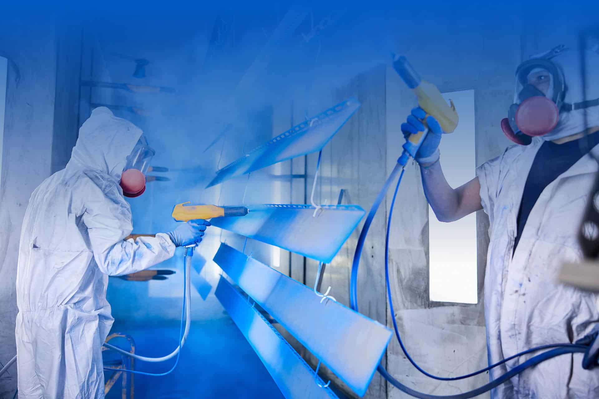 Workers spray painting large metal components in a factory setting.