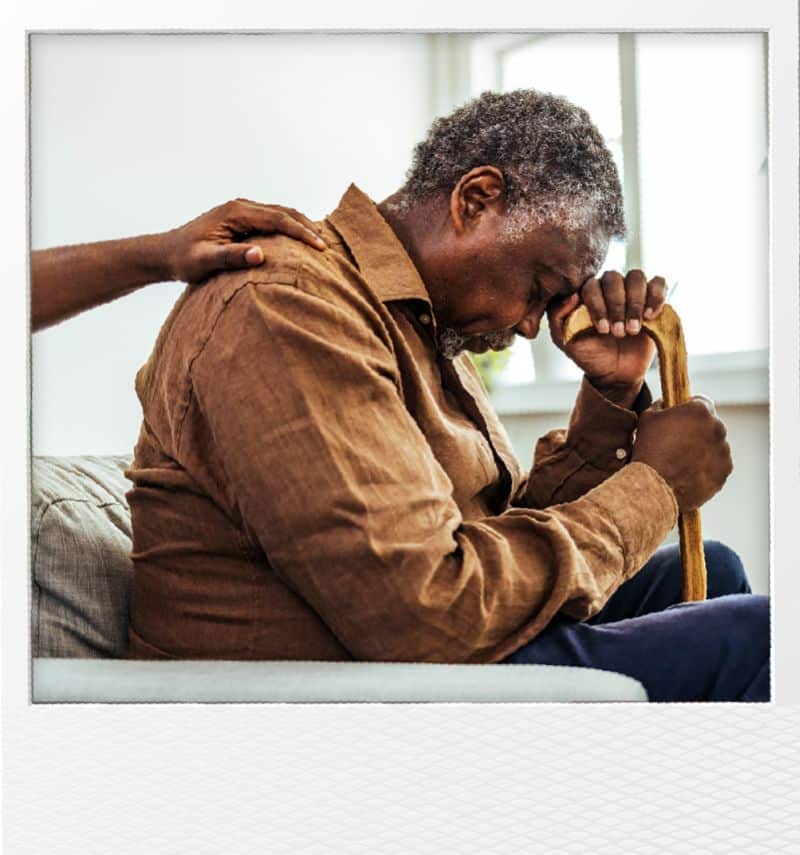 man with his head on a cane sitting down