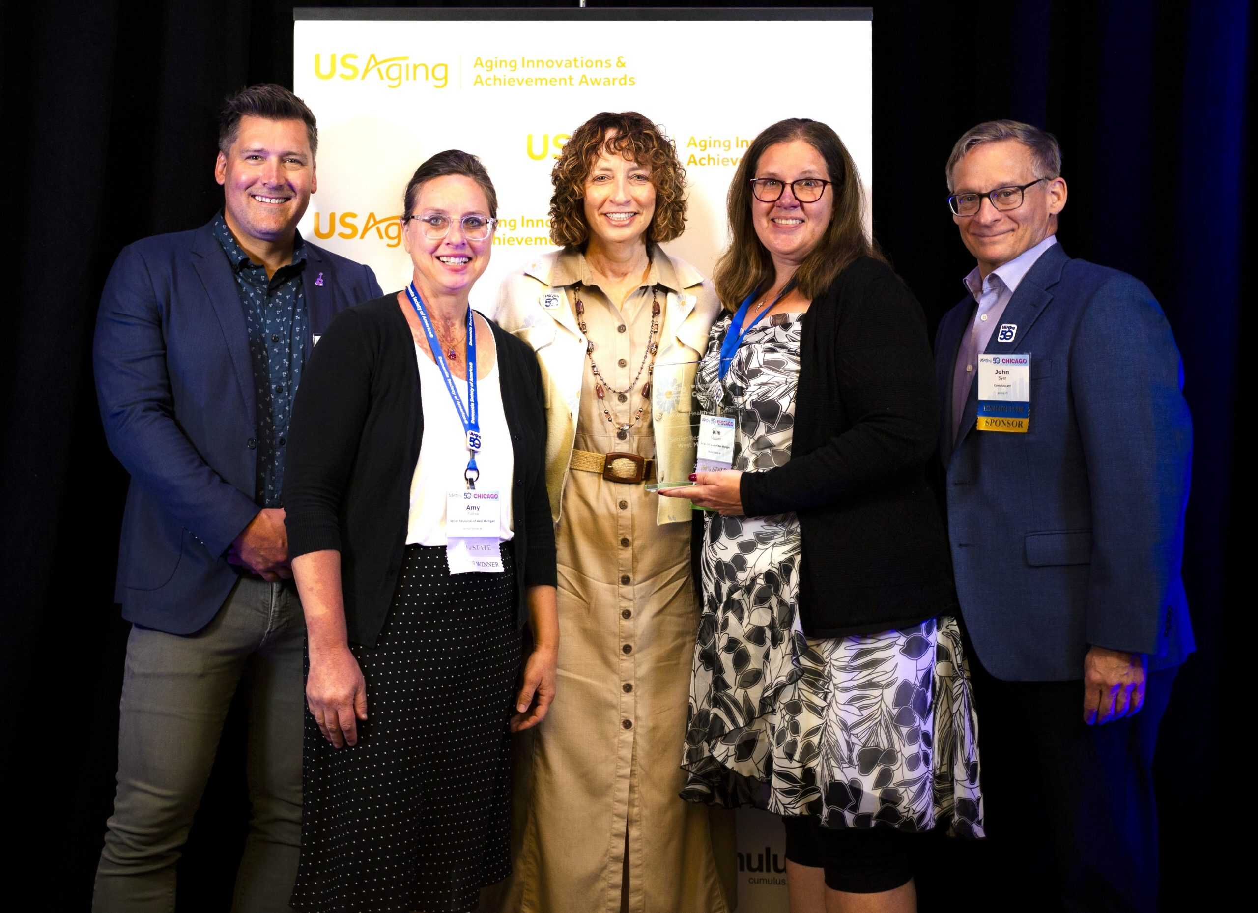 Group of five people at award ceremony with Senior Resources banner.