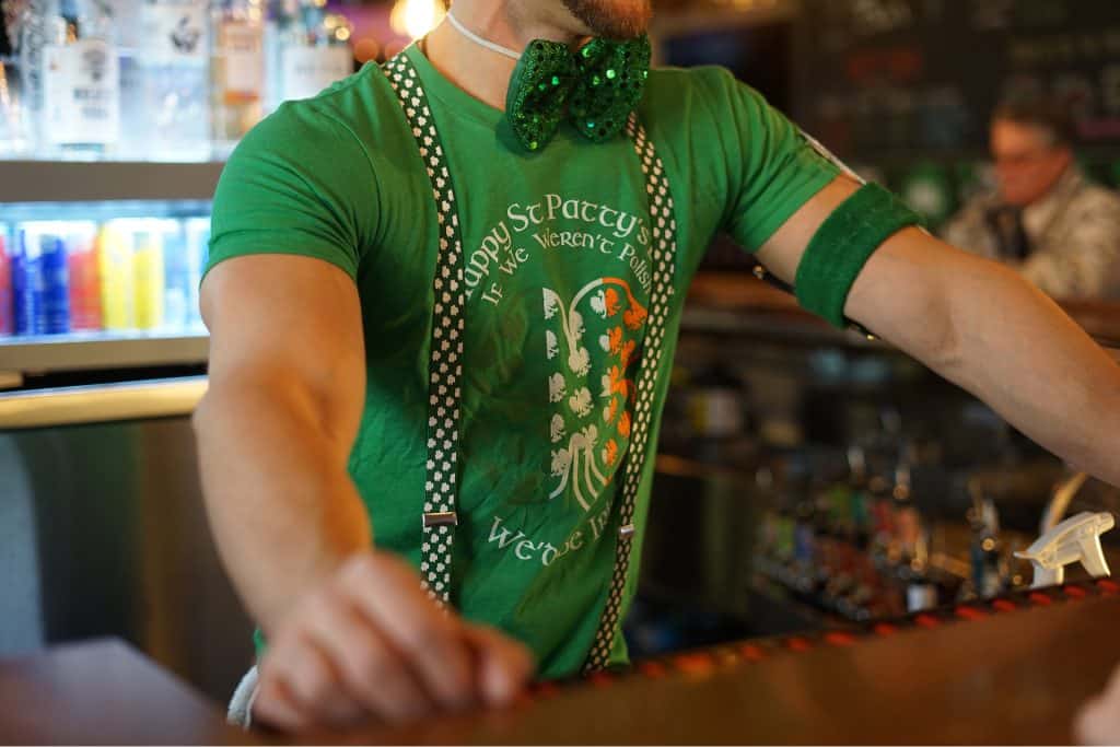 Bartender wearing green shamrock-themed outfit at bar.