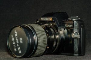Classic Minolta X-300s film camera with a zoom lens, set against a dark background, showcasing vintage photography equipment for nature and wildlife enthusiasts.