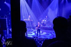 Concert A musical performance on stage with a band, featuring a guitarist and drummer, illuminated by vibrant blue stage lights, captured during a live concert.