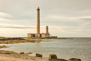 Lighthouse on rocky coastline under cloudy sky, maritime navigation, seascape photography.