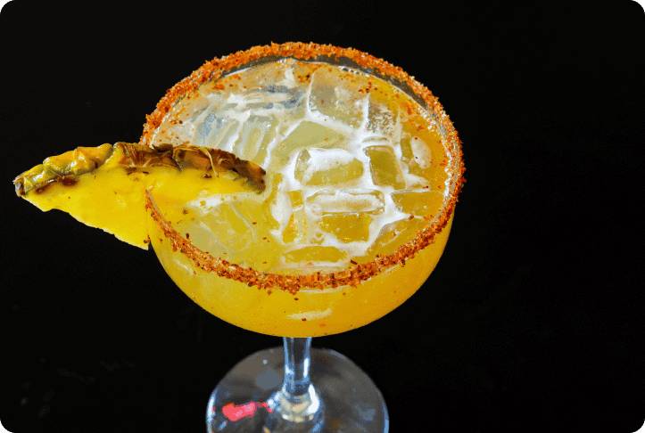 Lemon margarita cocktail with salted rim and pineapple garnish on black background.