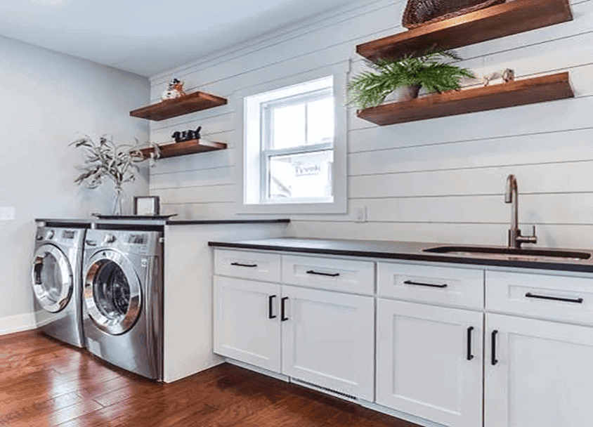 Contemporary laundry room with white cabinets, wooden shelves, and washer-dryer units.