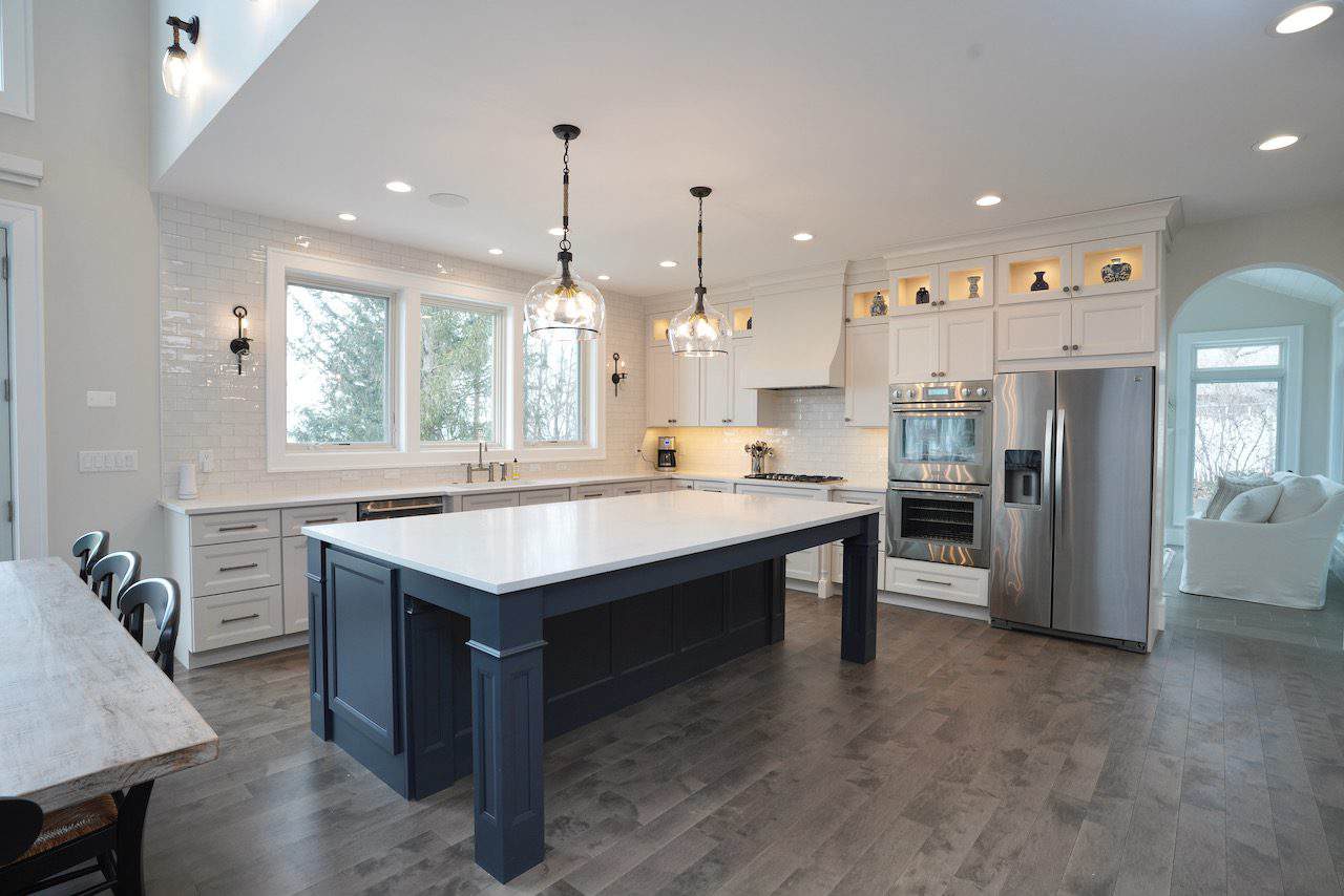Spacious modern kitchen with white cabinets, navy island, and stainless steel appliances.