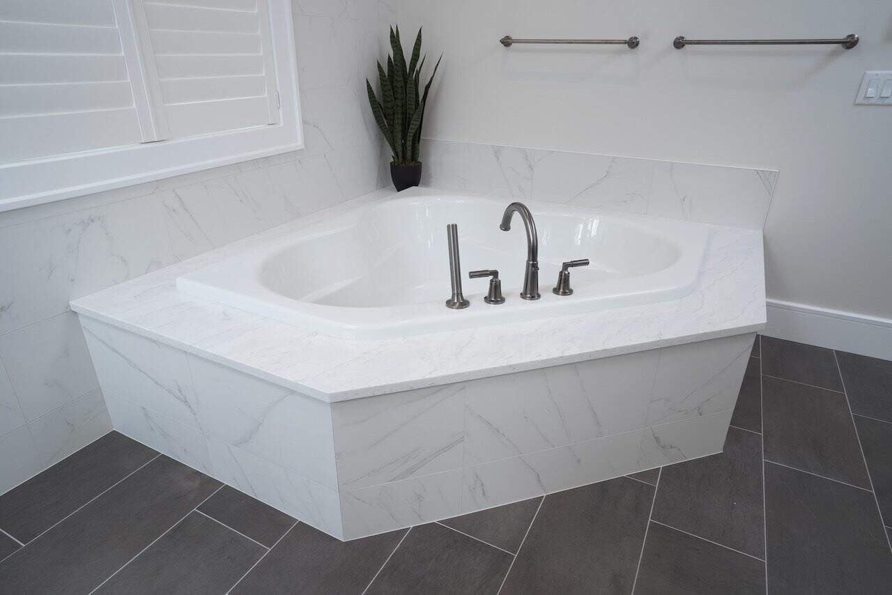 White marble corner bathtub with silver fixtures in a modern bathroom.