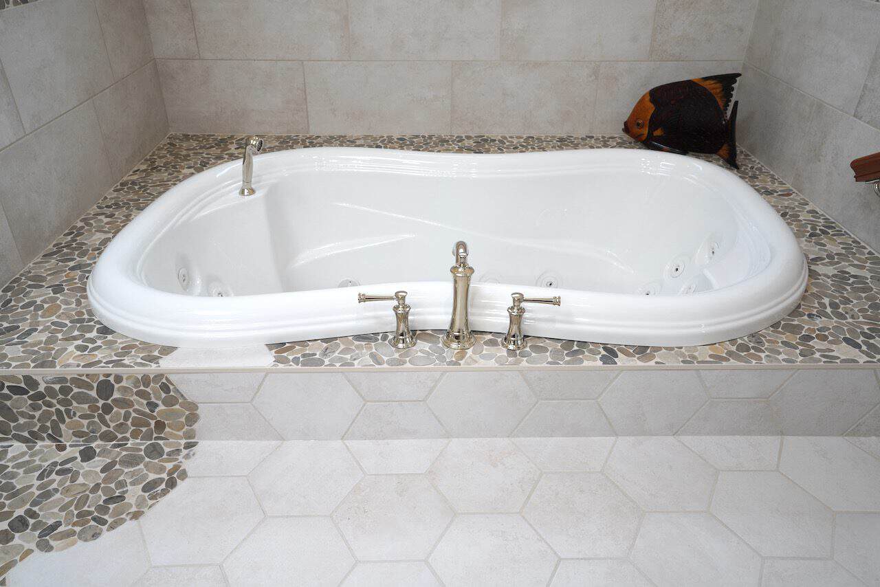 White built-in bathtub with chrome fixtures and pebble tile surround.