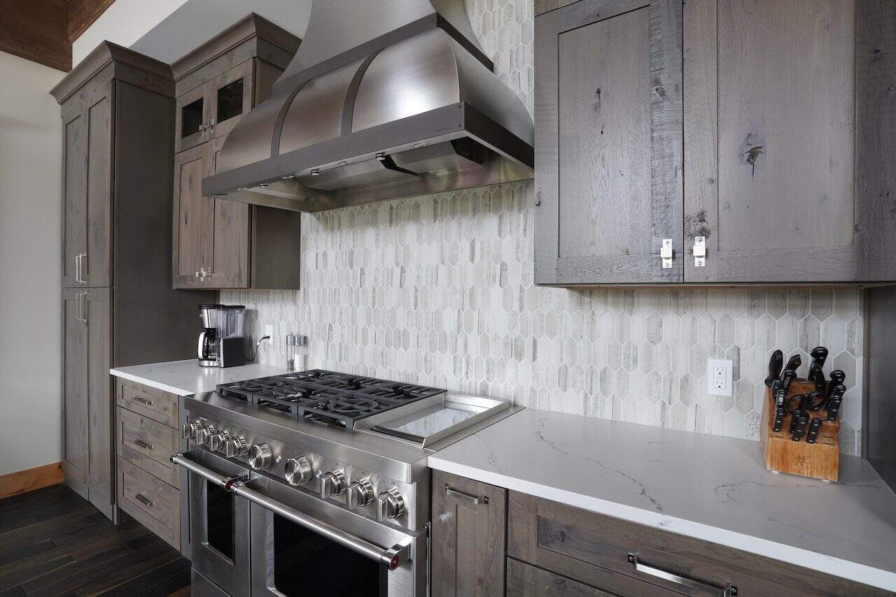 Contemporary kitchen with gray cabinets, stainless steel stove, and marble countertop.