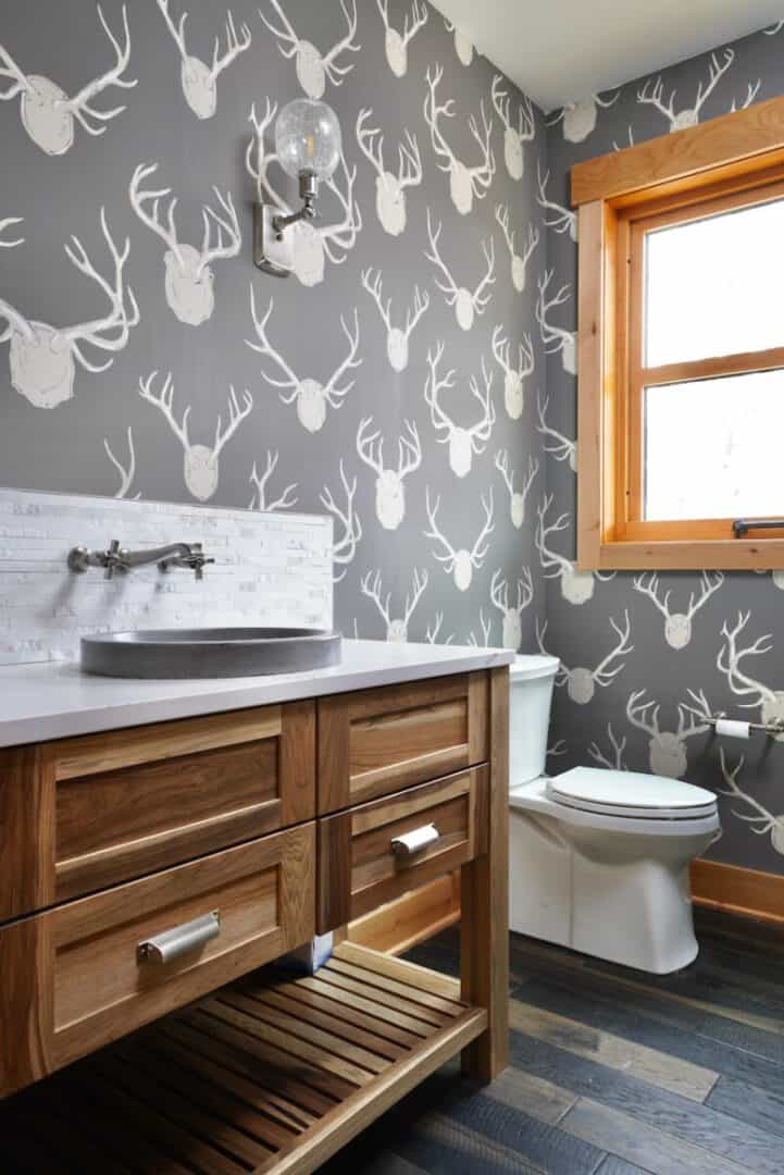 Bathroom with deer head wallpaper, wooden vanity, and white toilet.