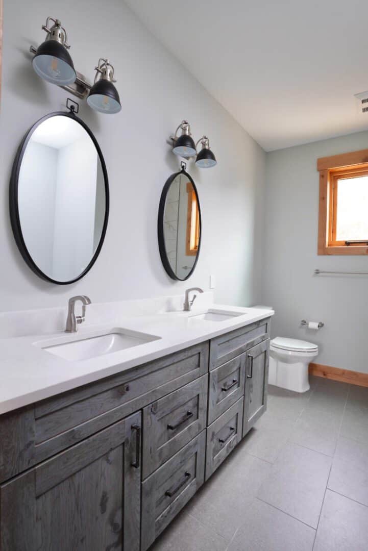 Contemporary bathroom with double sinks, oval mirrors, and wall-mounted lighting fixtures.