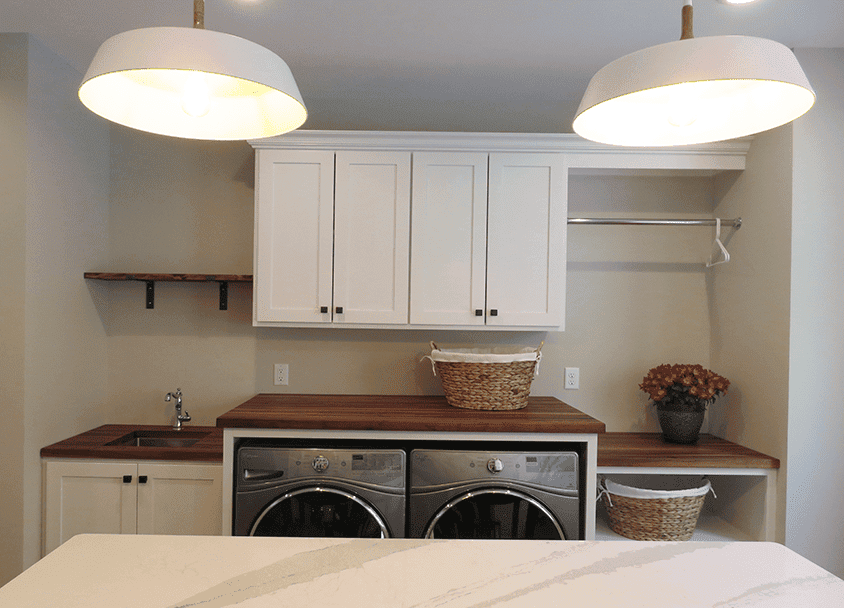 Clean laundry room with white cabinets, washer, dryer, and wooden countertops.