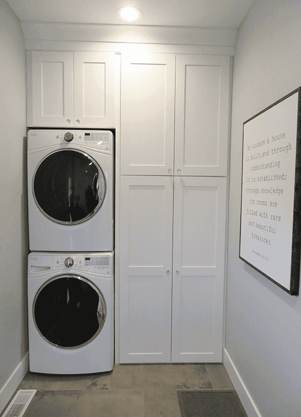 Laundry room with stacked washer and dryer and white storage cabinets.