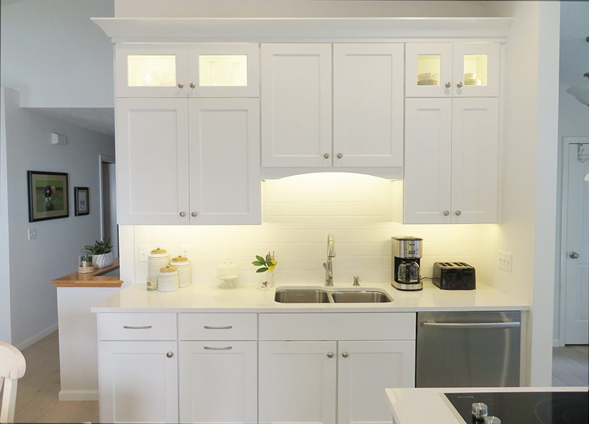 Bright white kitchen with upper and lower cabinets, stainless steel sink, and small appliances.