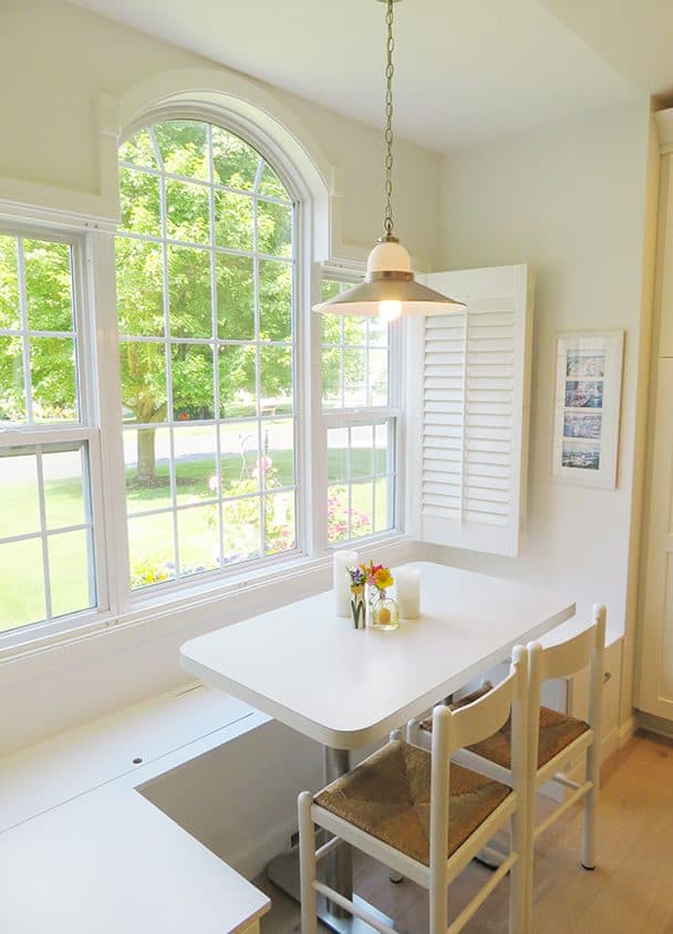 Sunlit kitchen corner with large arched window and white dining table with two chairs.