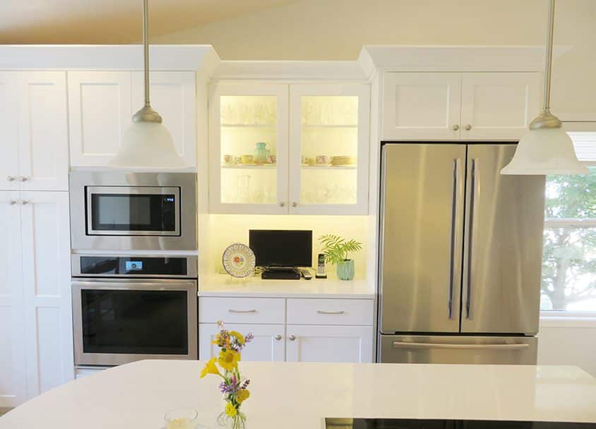Contemporary white kitchen with stainless steel refrigerator and built-in oven.