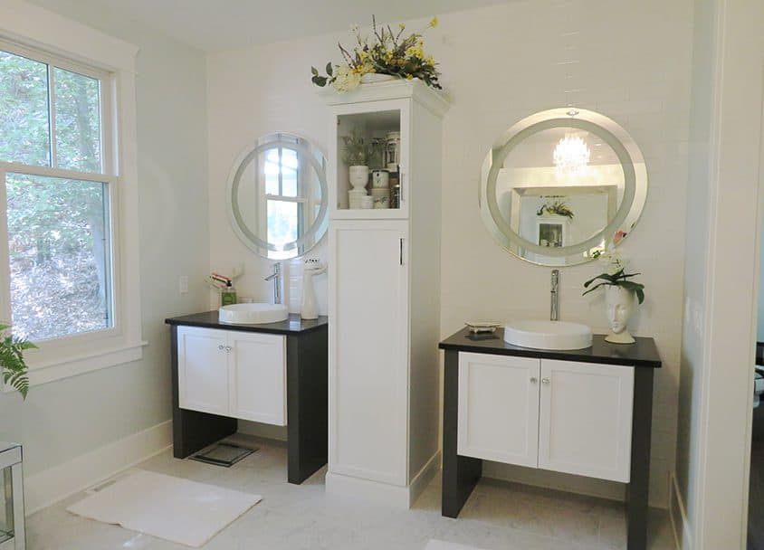 Contemporary bathroom with two white vanities, round mirrors, and a tall storage cabinet.