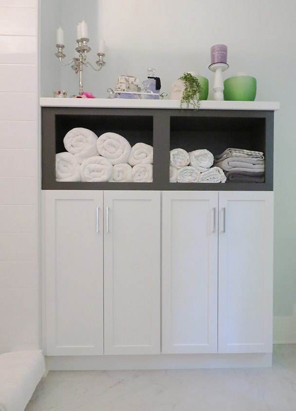 White bathroom storage cabinet with towels and decorative items on top.