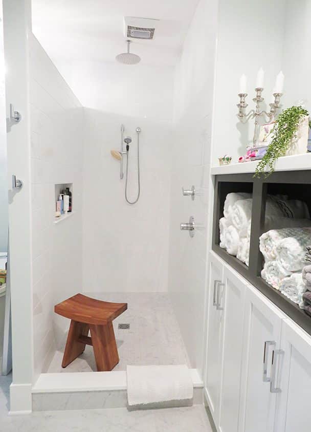 Minimalist white bathroom with walk-in shower and wooden stool.