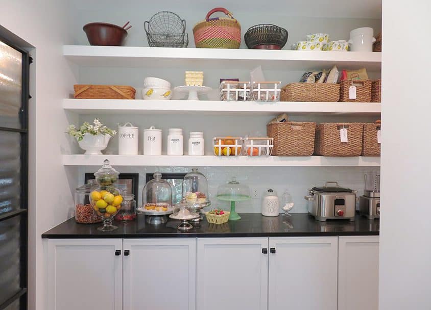 Kitchen shelves with baskets jars and appliances for storage.