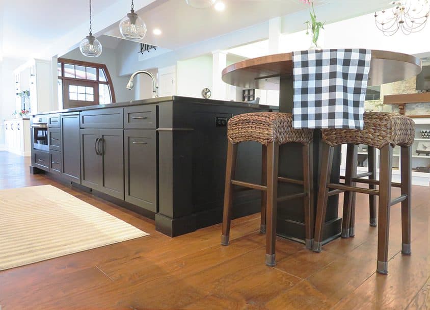 Contemporary kitchen with black cabinetry, wooden flooring, and a round island with checkered towel.