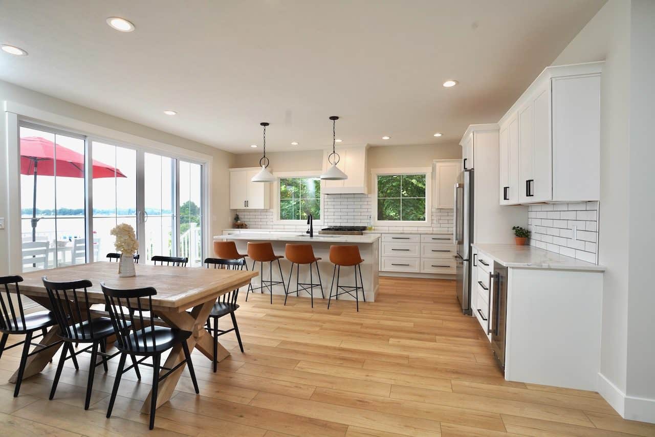 Spacious modern kitchen with white cabinets, wooden flooring, and a dining table with black chairs.