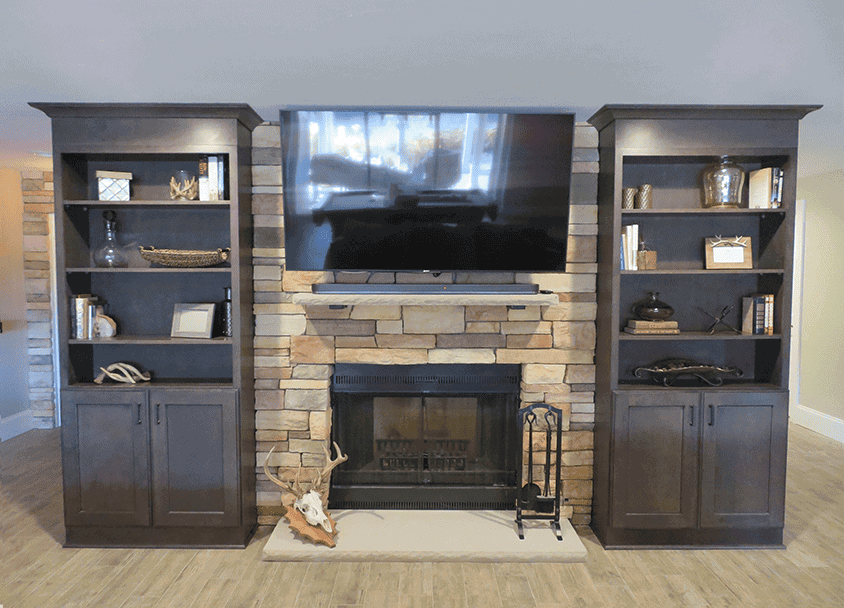 Living room with stone fireplace, TV, and dark wood shelves on each side.