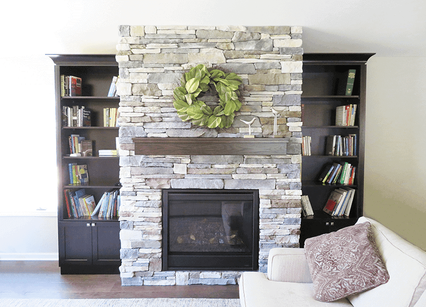 Stone fireplace with wooden mantel, green wreath, and black bookshelves on each side.
