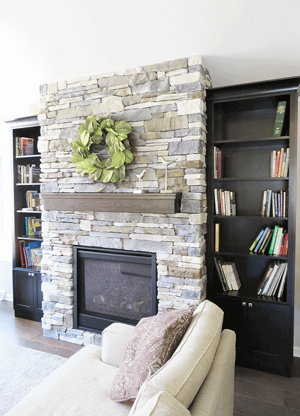 Stone fireplace with a green wreath and black bookshelves in a living room.