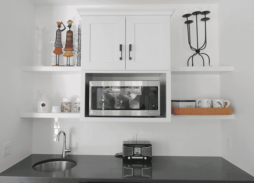 Contemporary kitchen with microwave, white cabinets, and open shelves.