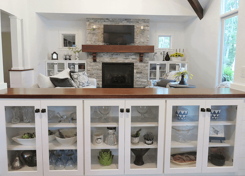 Bright kitchen with white cabinets and stone fireplace with TV above.