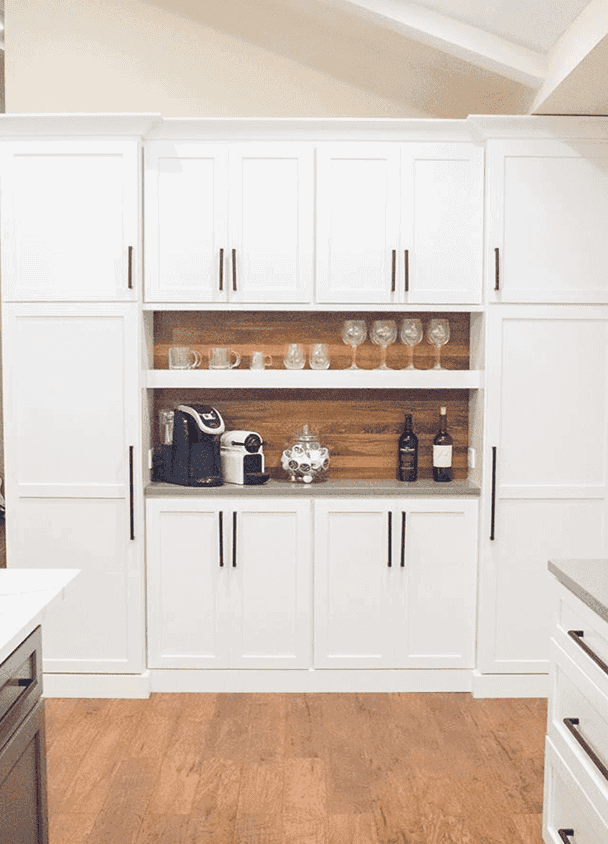 Modern white kitchen cabinets with open shelves and wine bottles display.