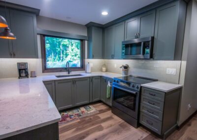 Contemporary kitchen with gray cabinets, stainless steel appliances, and a large window.