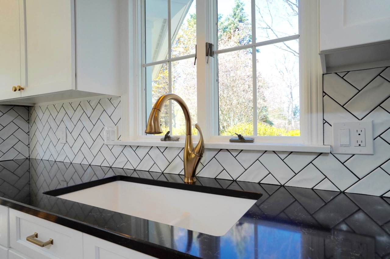 Kitchen sink with gold faucet and black countertop in bright kitchen.