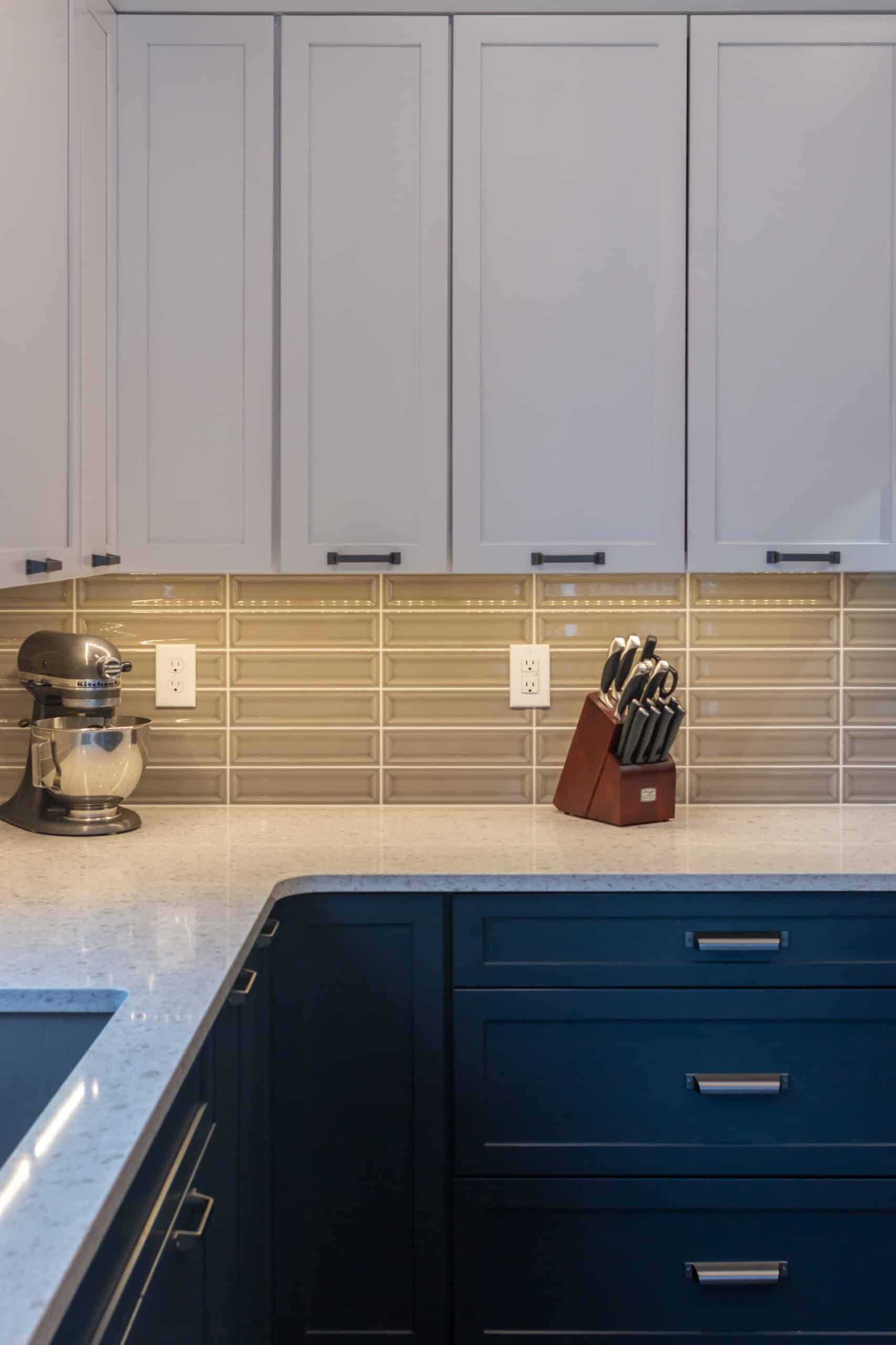 White upper cabinets with black handles and blue lower cabinets in a contemporary kitchen.