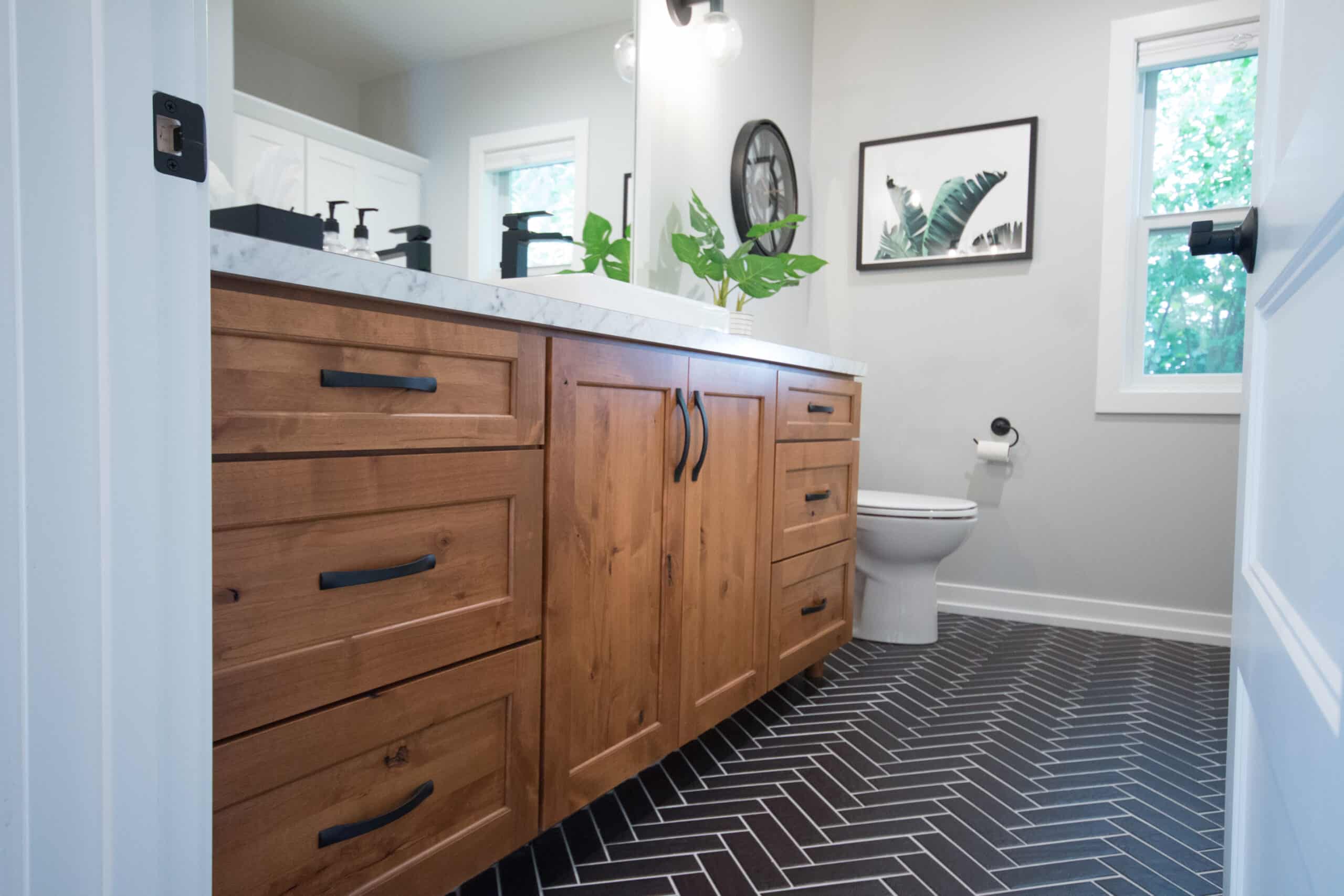 Bathroom with wooden vanity, black fixtures, and black herringbone tile floor.