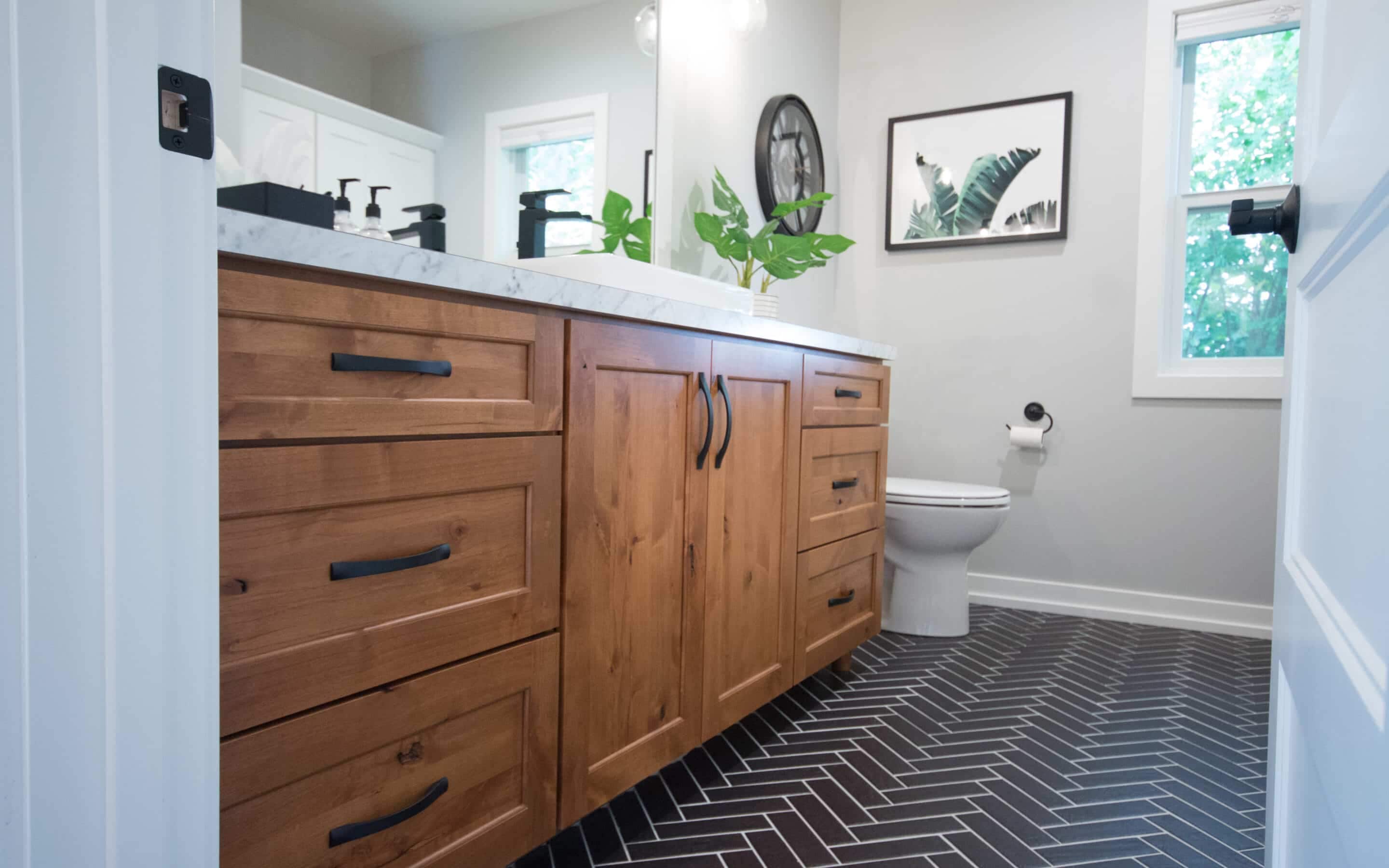 Contemporary bathroom with wooden vanity, black fixtures, and black herringbone tile floor.